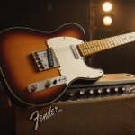Guitarra Fender Telecaster, com escudo preto e braço em maple, posicionada em pé sobre um suporte.
