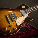 Guitarra Gibson Les Paul modelo Sunburst, com acabamento em verniz brilhante, dois captadores humbucker e escudo creme, posicionada sobre estojo aberto com forro aveludado vermelho.