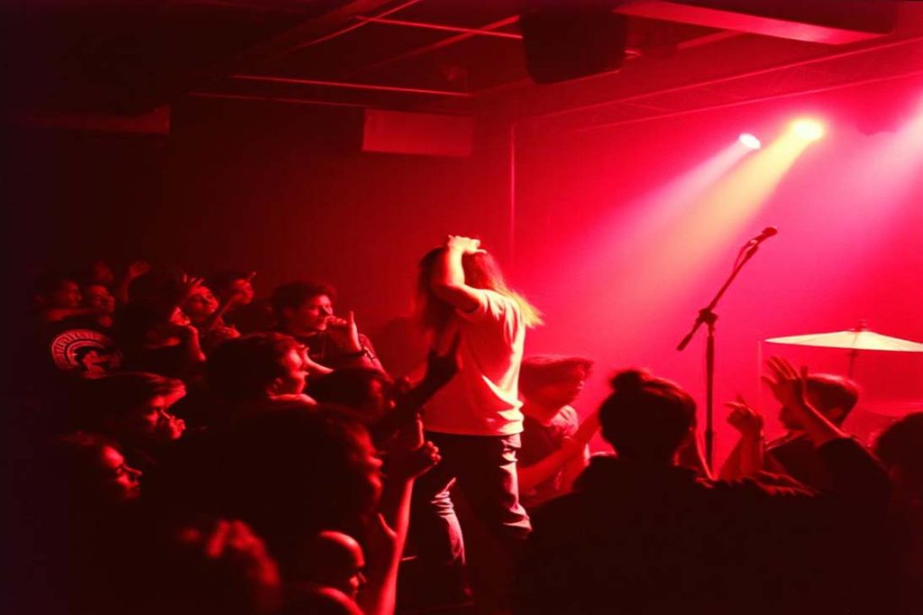 Banda grunge se apresentando ao vivo em palco pequeno, com público próximo e atmosfera intensa e escura.