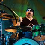 Jason Bonham tocando bateria em show tributo ao Led Zeppelin, com bateria verde metálica, usando touca e óculos escuros.