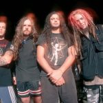 Integrantes da formação clássica da banda Sepultura posam em frente a caminhões, com roupas alternativas e visual característico do metal dos anos 90.